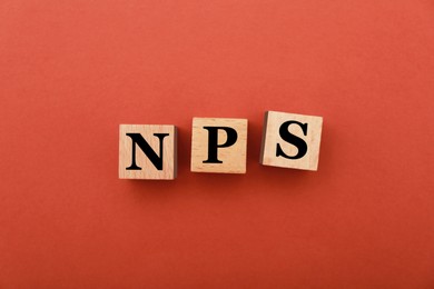 Image of NPS (net promoter score) abbreviation made of wooden cubes on red background, top view