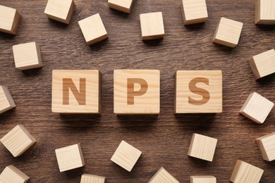 Image of NPS (net promoter score) abbreviation made of cubes on wooden table, top view