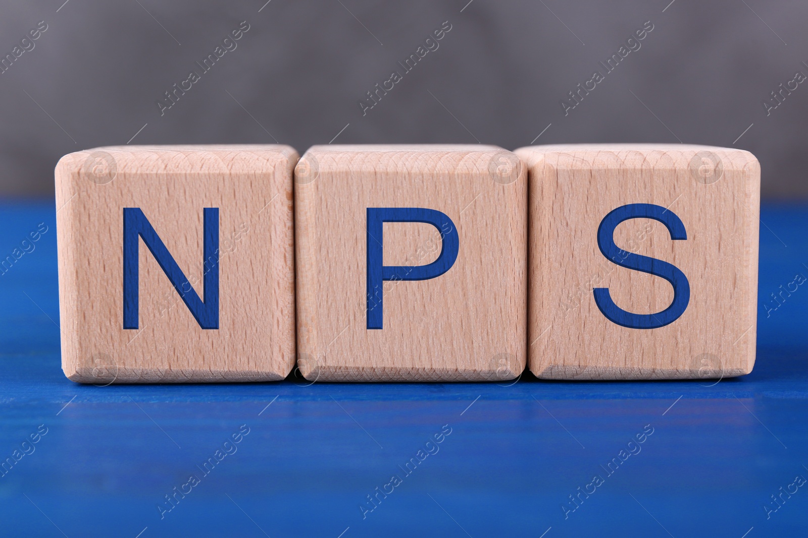 Image of NPS (net promoter score) abbreviation made of cubes on blue wooden table