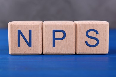 Image of NPS (net promoter score) abbreviation made of cubes on blue wooden table