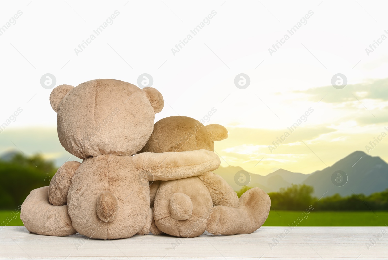 Image of Hugging teddy bears on wooden surface looking at picturesque mountain landscape, back view. Space for text