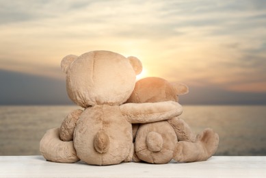 Image of Hugging teddy bears on wooden surface looking at picturesque seascape, back view