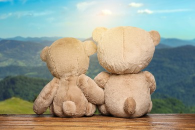 Image of Fluffy teddy bears on wooden surface looking at picturesque mountain landscape, back view