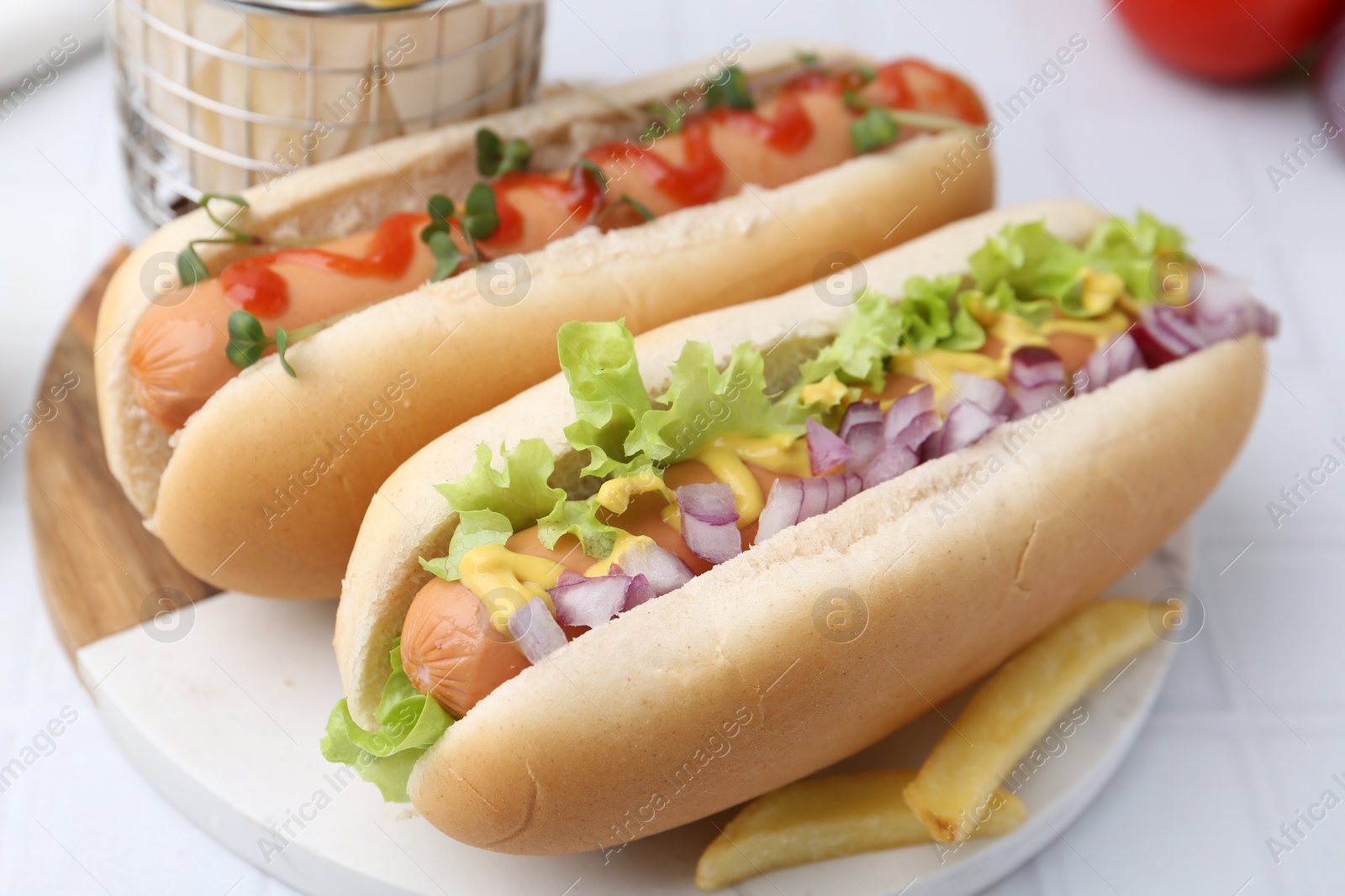 Photo of Tasty hot dogs served on white tiled table, closeup