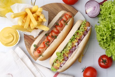 Photo of Tasty hot dogs served on white tiled table, flat lay