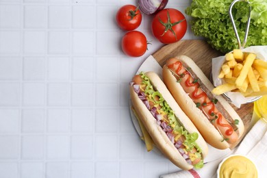 Photo of Tasty hot dogs served on white tiled table, flat lay. Space for text