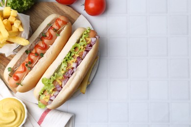 Photo of Tasty hot dogs served on white tiled table, flat lay. Space for text