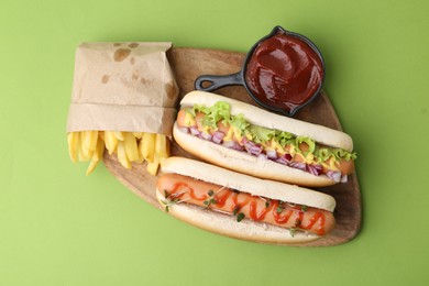 Photo of Tasty hot dogs with fries and ketchup on green background, top view