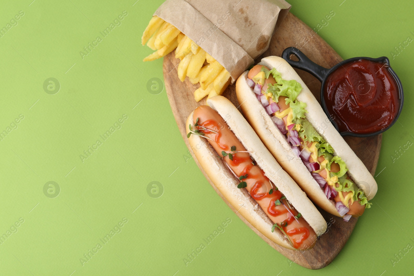 Photo of Tasty hot dogs with fries and ketchup on green background, top view. Space for text