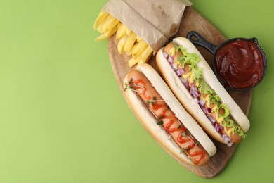 Photo of Tasty hot dogs with fries and ketchup on green background, top view. Space for text