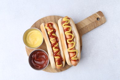 Photo of Tasty hot dogs with ketchup and mustard on light table, top view