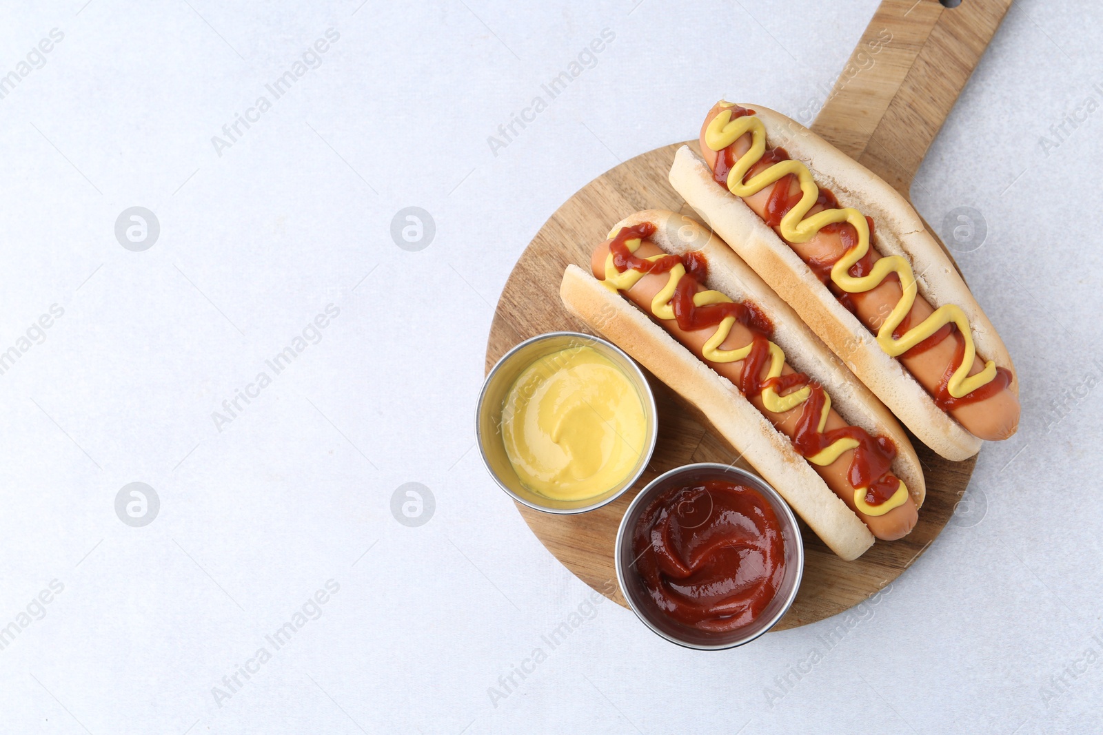 Photo of Tasty hot dogs with ketchup and mustard on light table, top view. Space for text