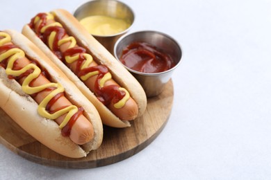 Photo of Tasty hot dogs with ketchup and mustard on light table, closeup