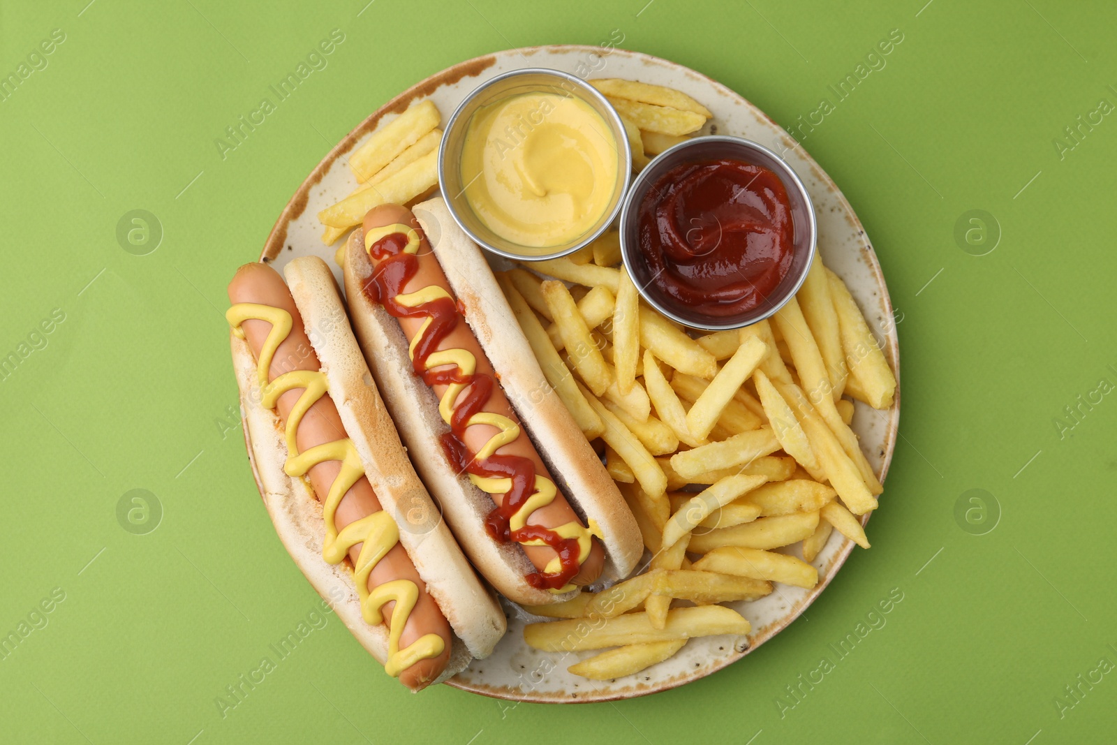 Photo of Tasty hot dogs with fries and sauces on green background, top view