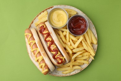 Photo of Tasty hot dogs with fries and sauces on green background, top view