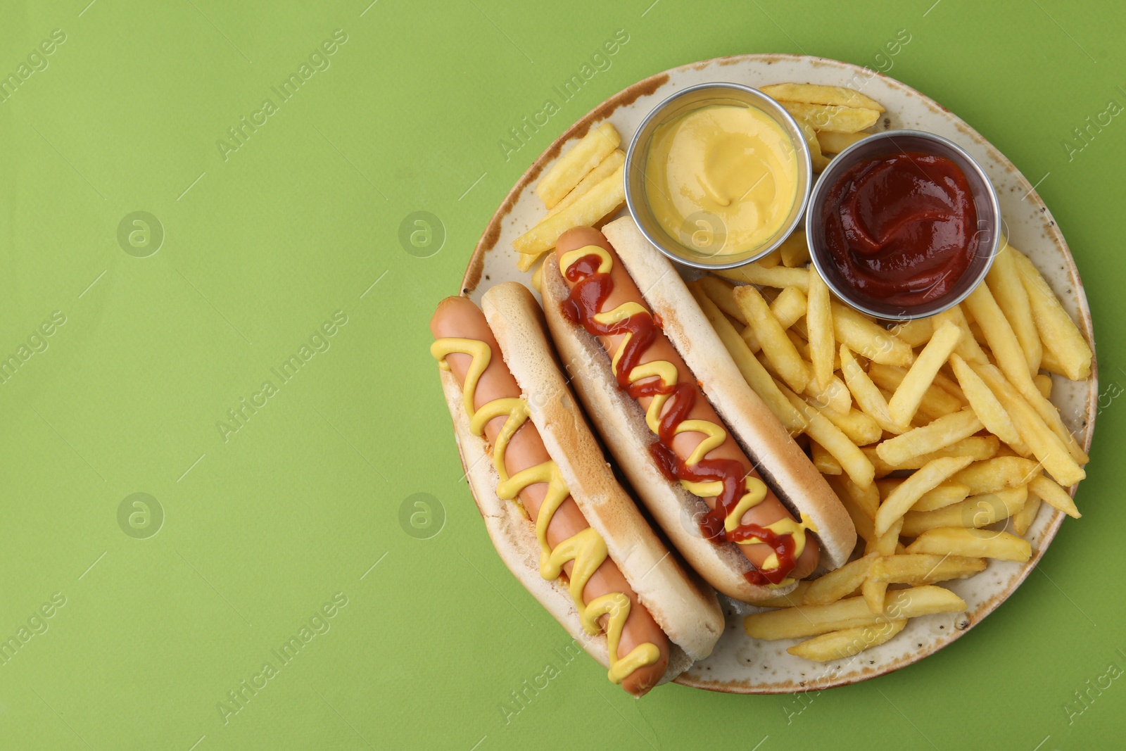 Photo of Tasty hot dogs with fries and sauces on green background, top view. Space for text