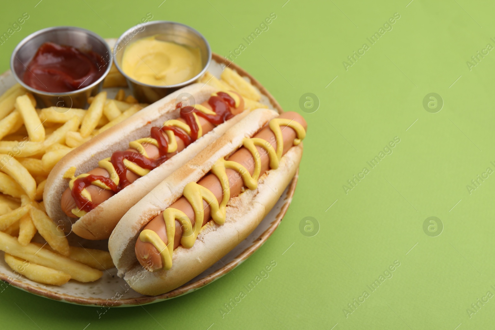 Photo of Tasty hot dogs with fries and sauces on green background, closeup. Space for text