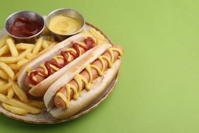 Photo of Tasty hot dogs with fries and sauces on green background, closeup. Space for text