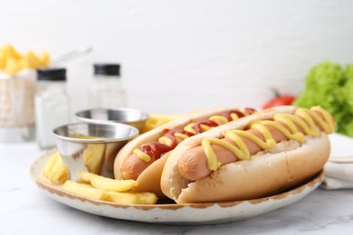 Photo of Tasty hot dogs with fries served on white marble table, closeup