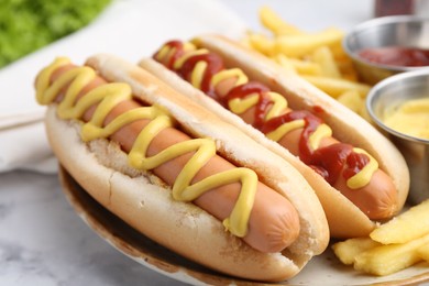 Photo of Tasty hot dogs with fries on white marble table, closeup