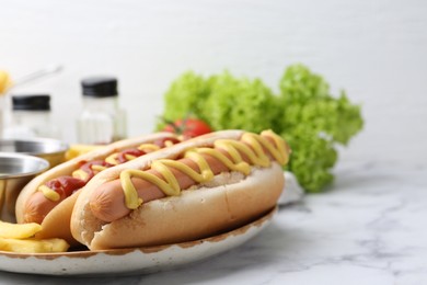 Photo of Tasty hot dogs with fries on white marble table, closeup