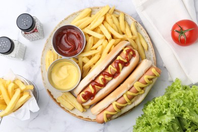 Photo of Tasty hot dogs with fries served on white marble table, flat lay