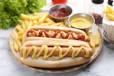 Photo of Tasty hot dogs with fries served on white marble table, closeup