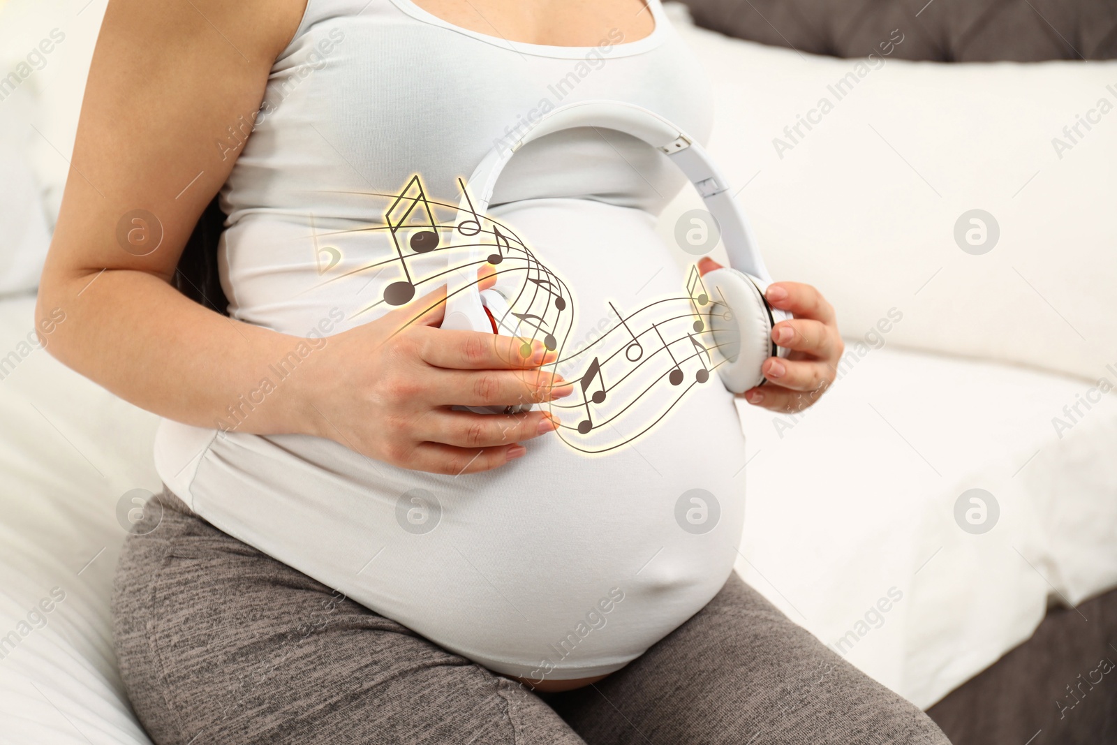 Image of Pregnant woman holding headphones near her belly at home, closeup. Music notes flying around