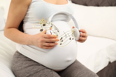 Image of Pregnant woman holding headphones near her belly at home, closeup. Music notes flying around