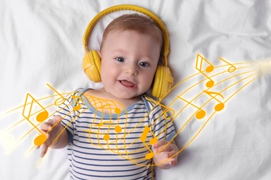 Image of Cute little baby with headphones lying on bed, top view. Music notes flying around