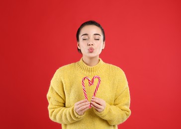 Photo of Young woman in yellow sweater holding candy canes on red background. Celebrating Christmas