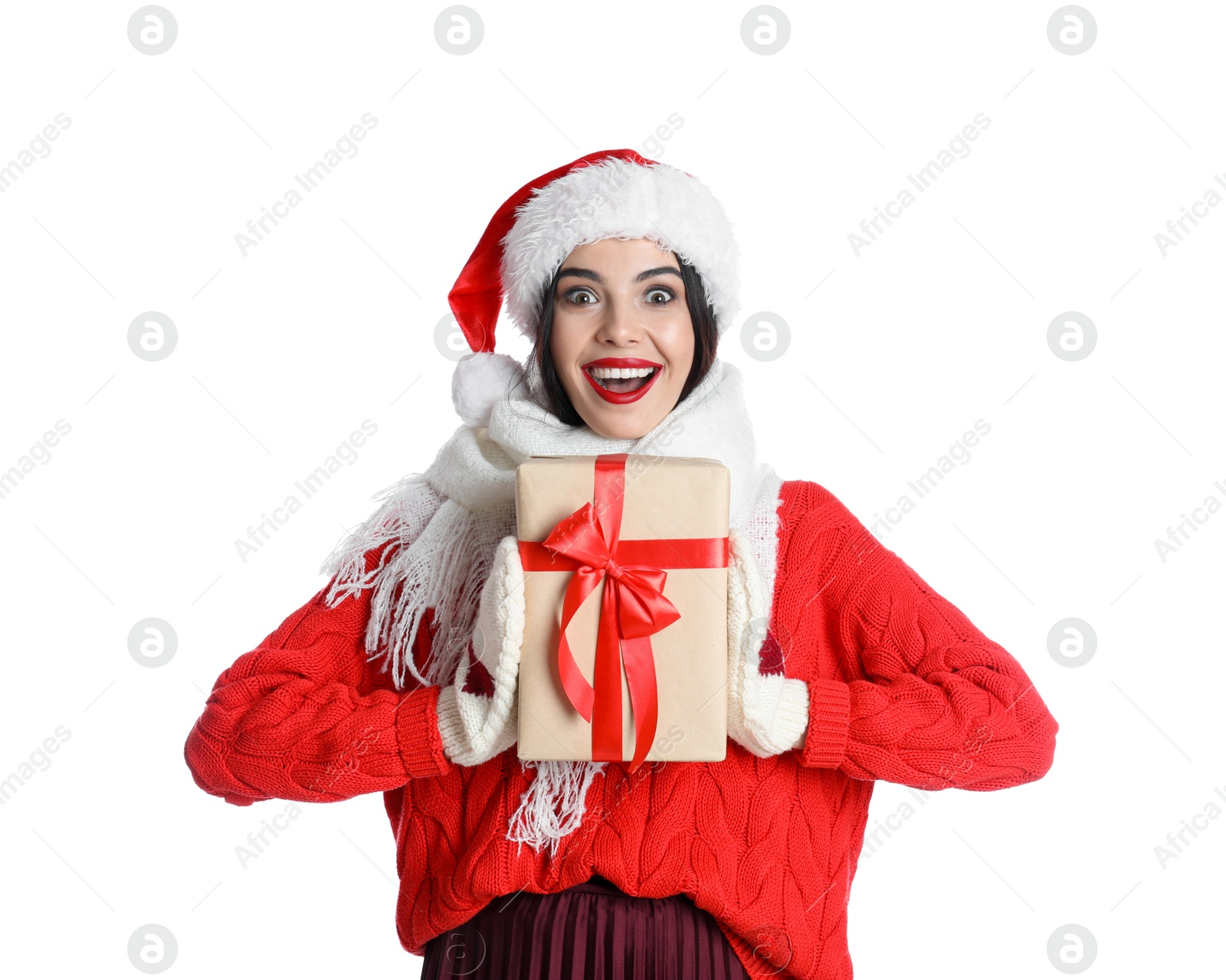 Photo of Excited woman in Santa hat, knitted mittens, scarf and red sweater holding Christmas gift on white background