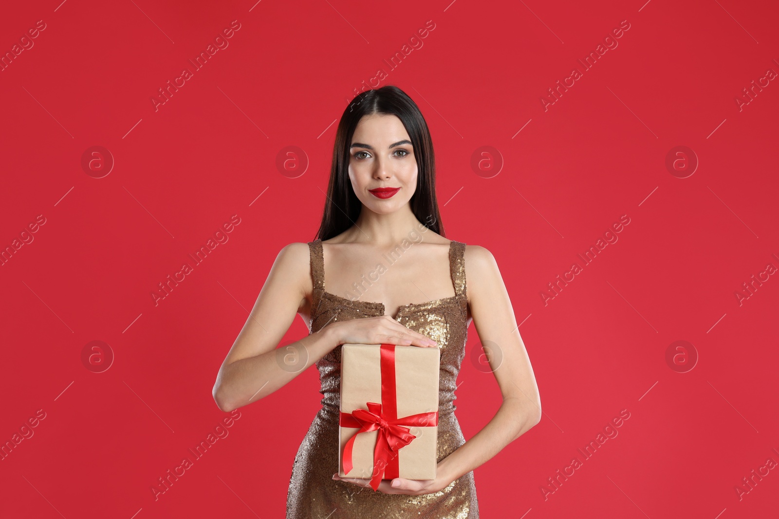 Photo of Woman in golden dress holding Christmas gift on red background