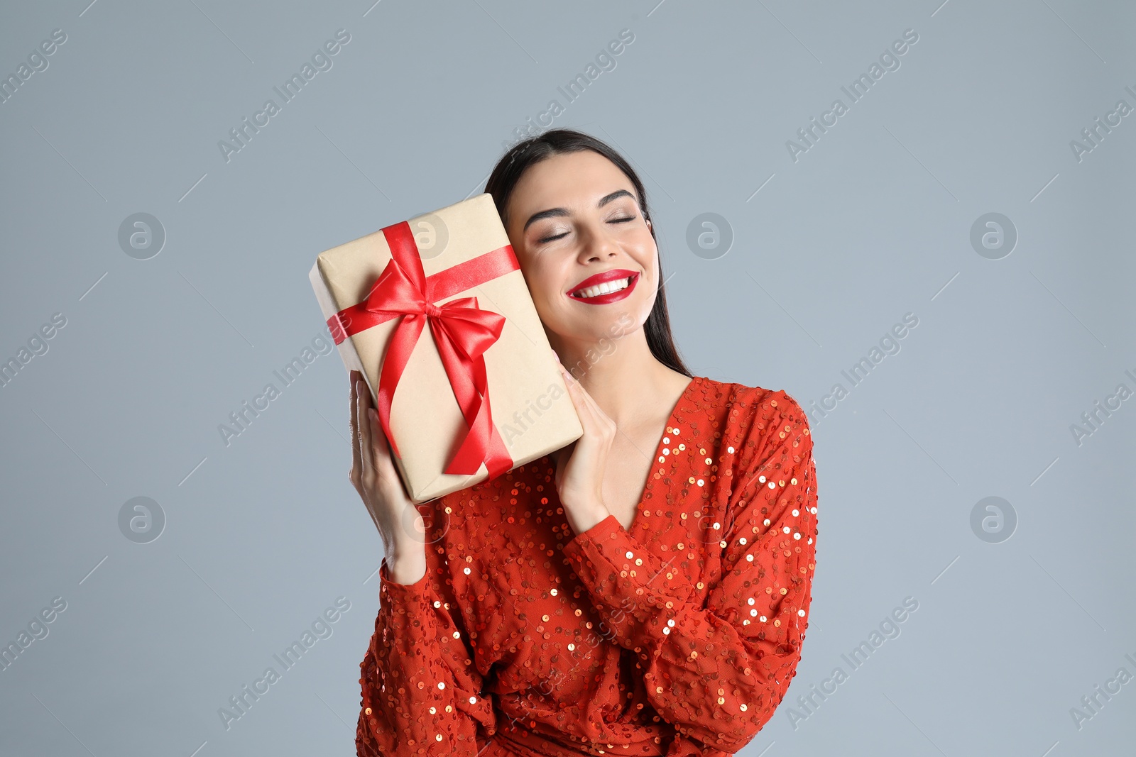 Photo of Woman in red dress holding Christmas gift on grey background