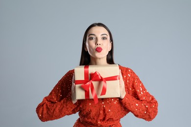 Photo of Woman in red dress holding Christmas gift on grey background