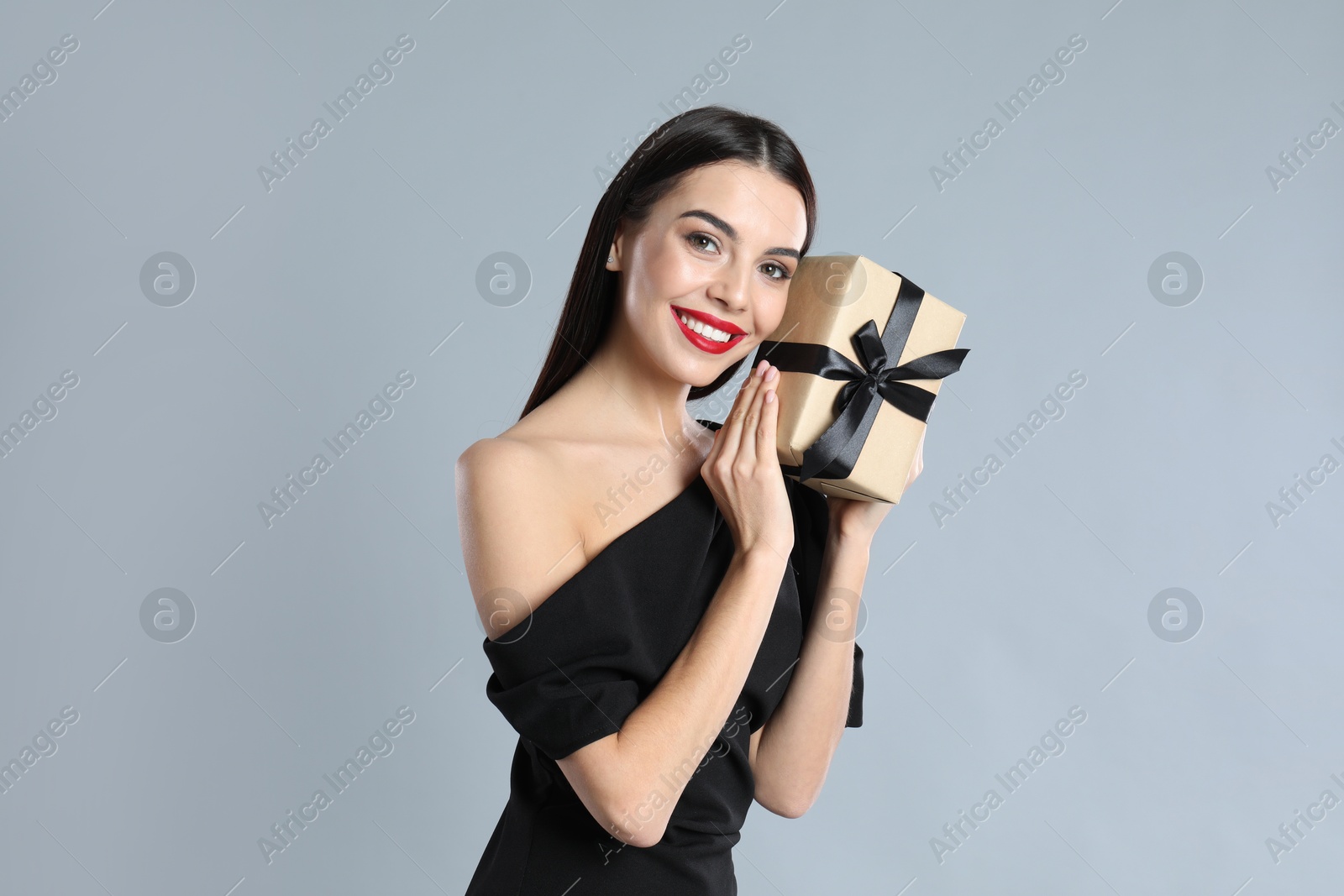 Photo of Woman in black dress holding Christmas gift on grey background