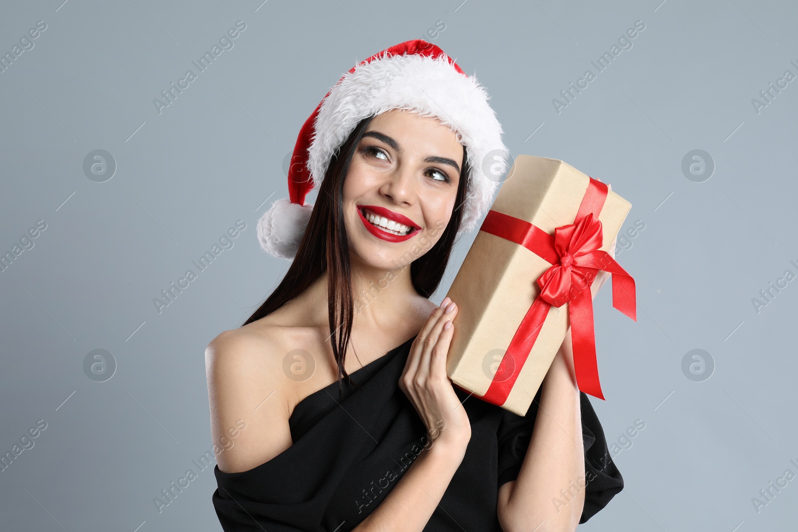 Photo of Woman in black dress and Santa hat holding Christmas gift on grey background