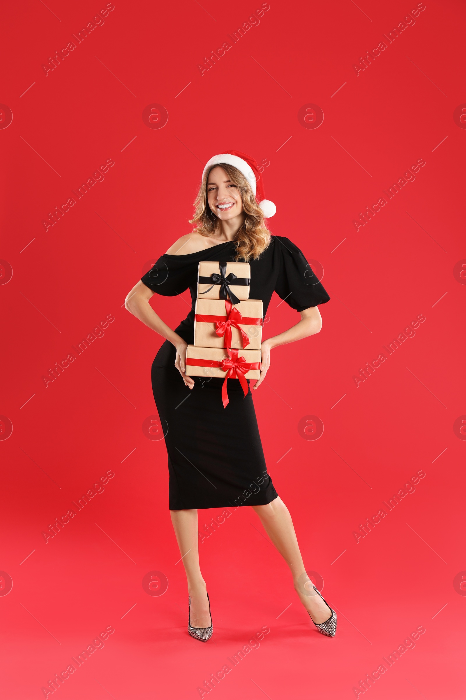 Photo of Beautiful young woman in Santa hat with Christmas presents on red background