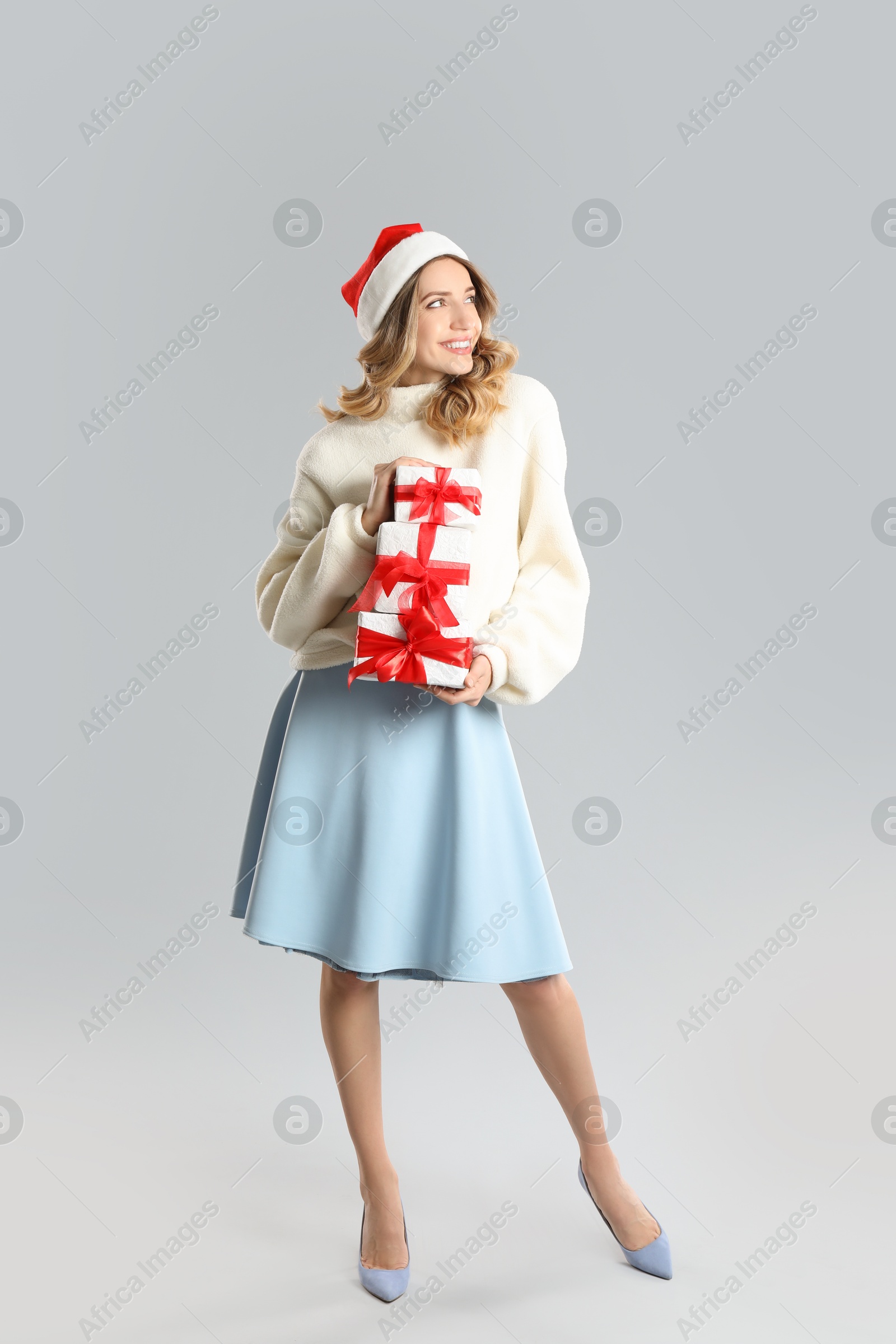 Photo of Beautiful young woman in Santa hat with Christmas presents on light grey background