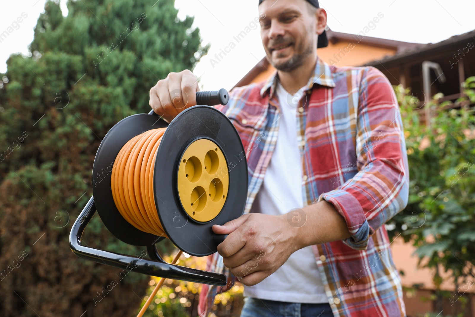 Photo of Man with extension cord reel outdoors, selective focus