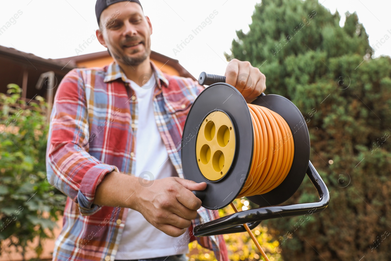 Photo of Man with extension cord reel outdoors, selective focus