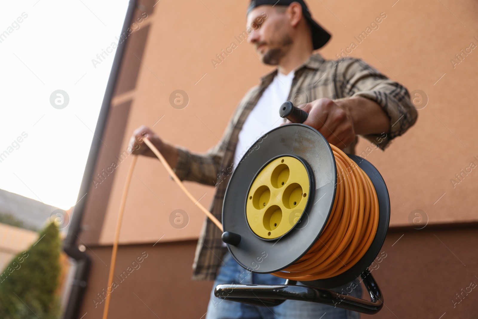 Photo of Man with extension cord reel outdoors, selective focus