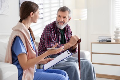 Photo of Caregiver examining senior man on sofa indoors. Home health care service