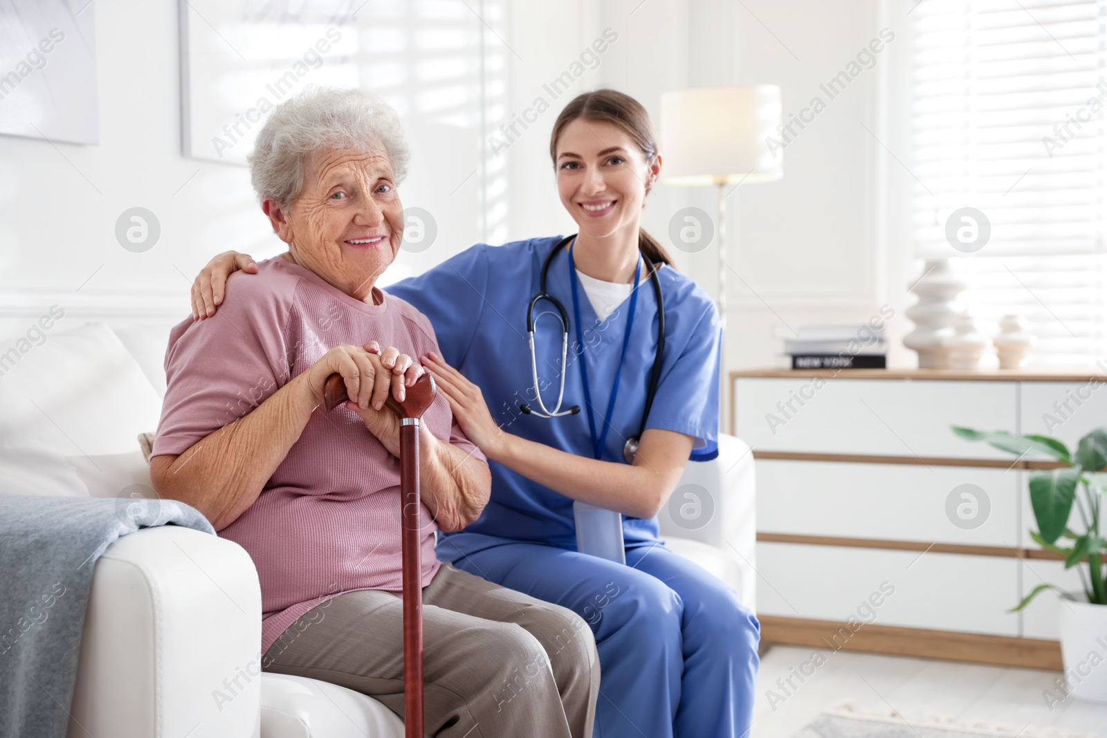 Photo of Caregiver supporting senior woman on sofa. Home health care service