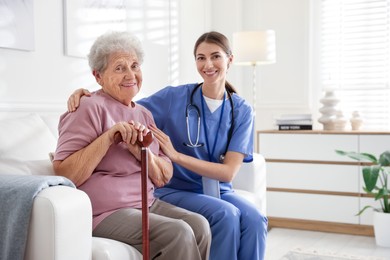 Photo of Caregiver supporting senior woman on sofa. Home health care service