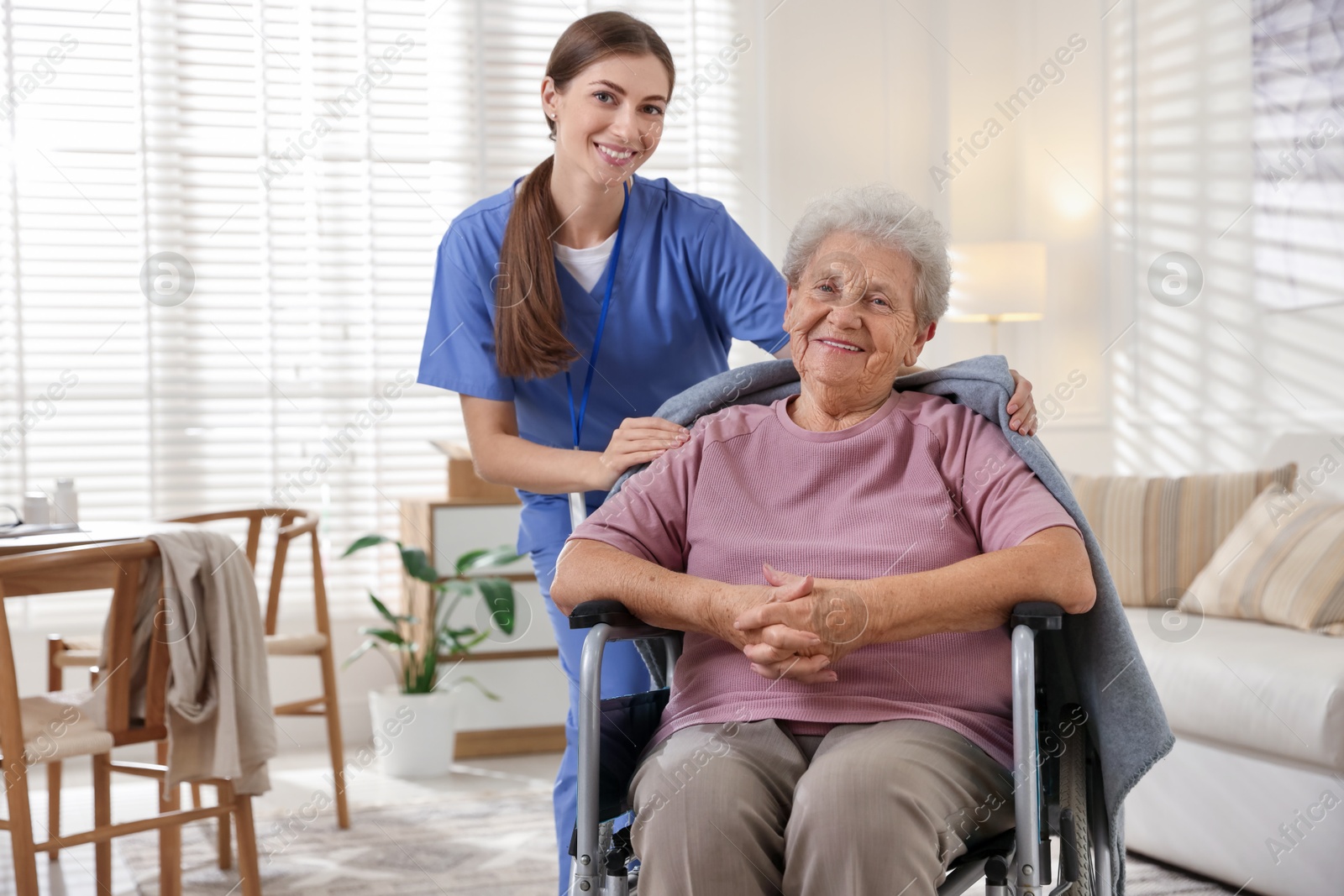 Photo of Caregiver covering senior woman with blanket indoors. Home health care service