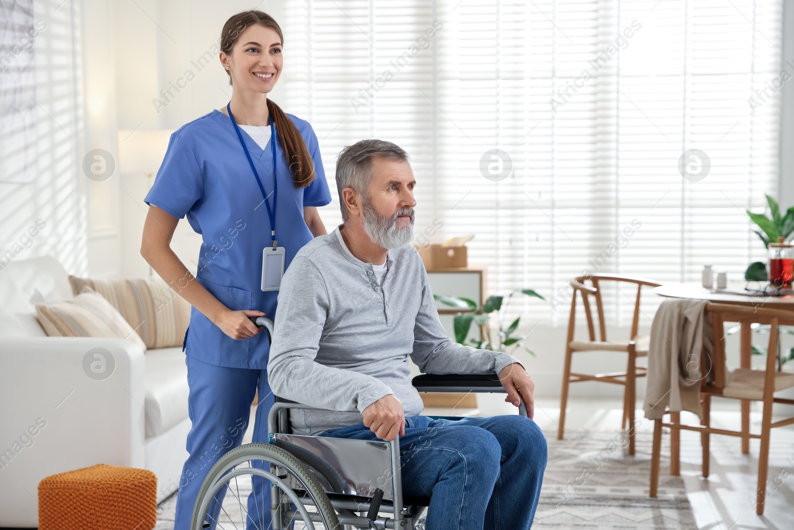 Photo of Caregiver assisting senior man in wheelchair indoors. Home health care service