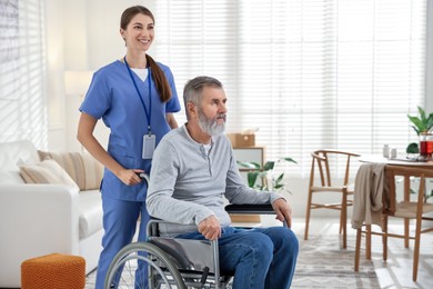 Photo of Caregiver assisting senior man in wheelchair indoors. Home health care service