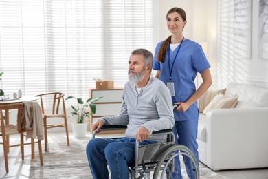 Photo of Caregiver assisting senior man in wheelchair indoors. Home health care service