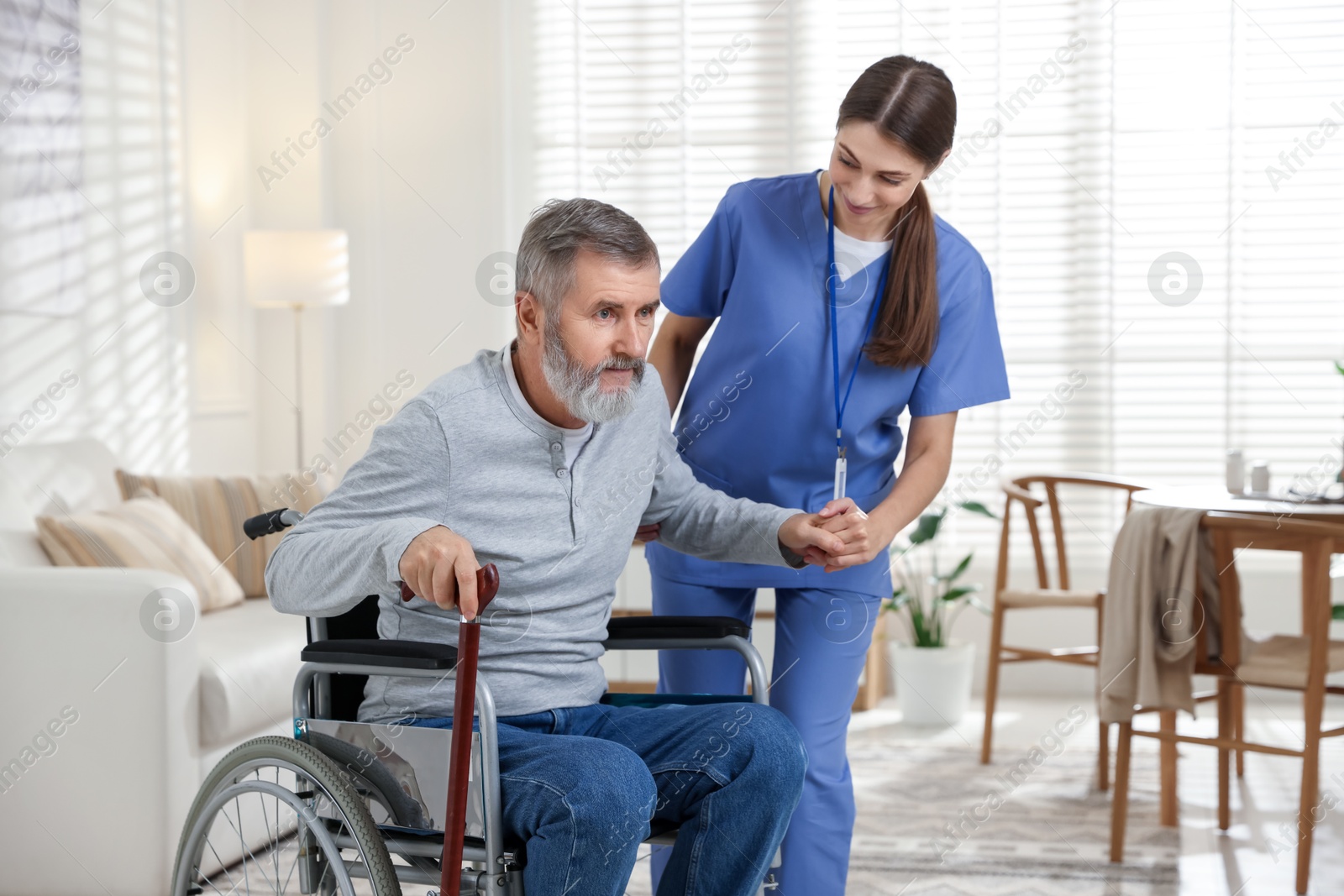 Photo of Caregiver assisting senior man in wheelchair indoors. Home health care service